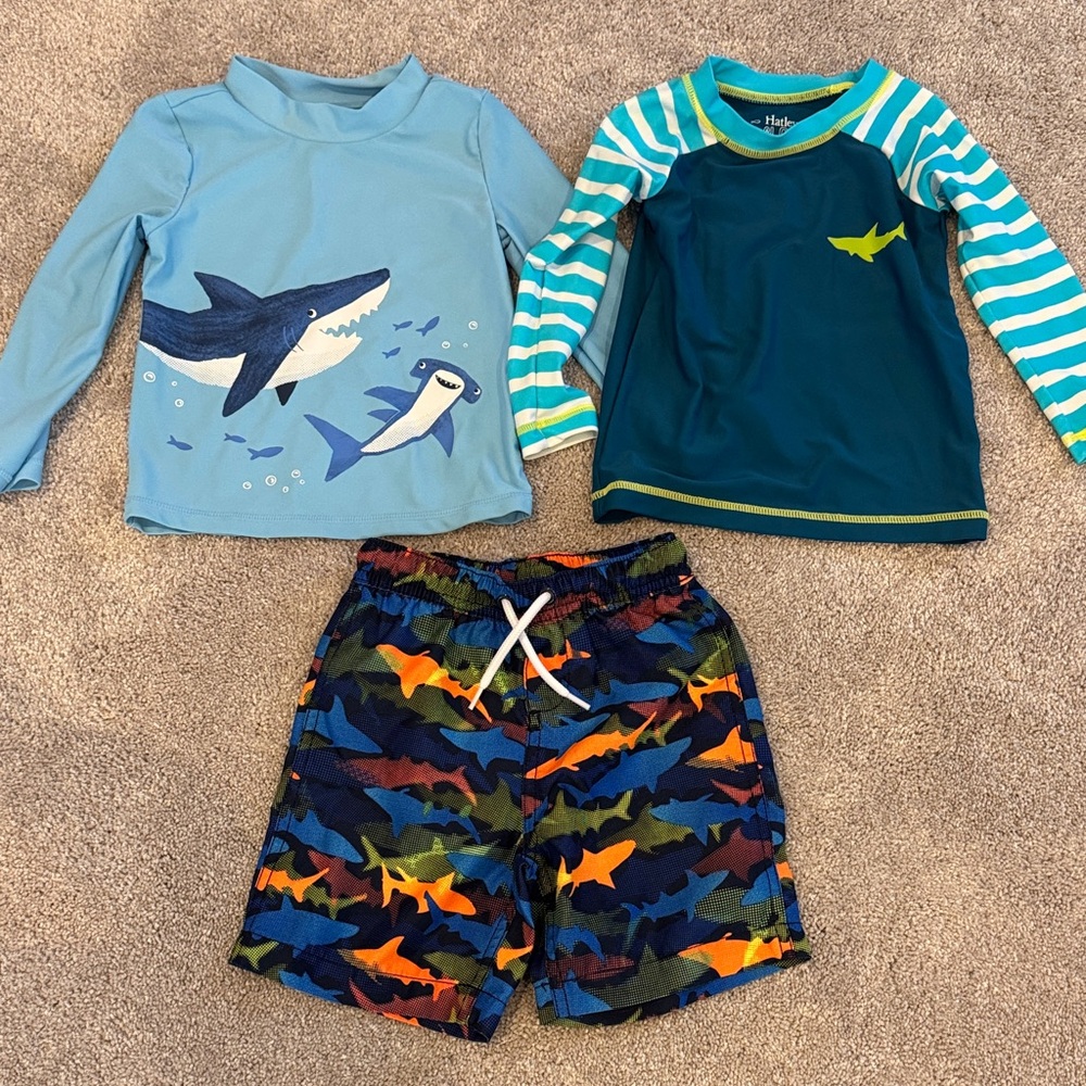 2 kids rash guards and one shark swim trunks